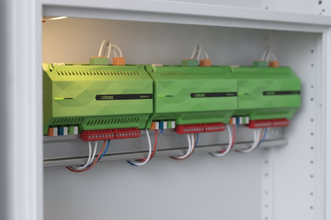 Drei Loxone Miniserver nebeneinander auf einer Hutschiene im Verteilerschrank, der erste warm beleuchtet